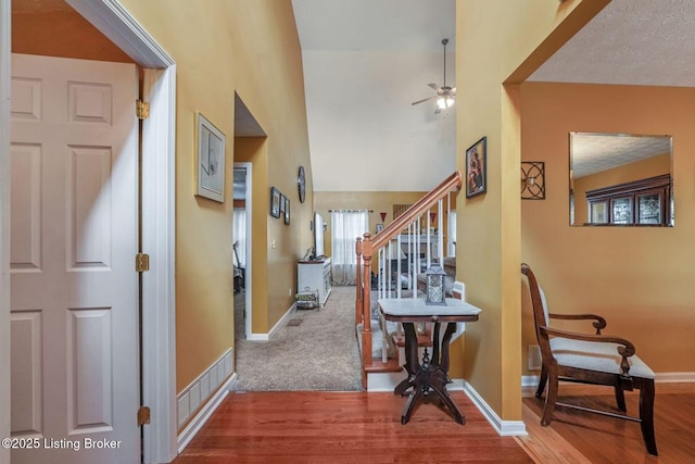 corridor with stairs, a high ceiling, wood finished floors, and baseboards