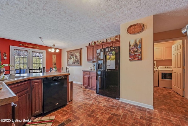 kitchen with baseboards, brick floor, washer and dryer, black appliances, and a sink