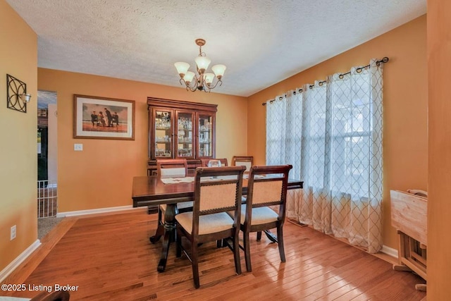 dining space with a chandelier, baseboards, a textured ceiling, and light wood-style floors