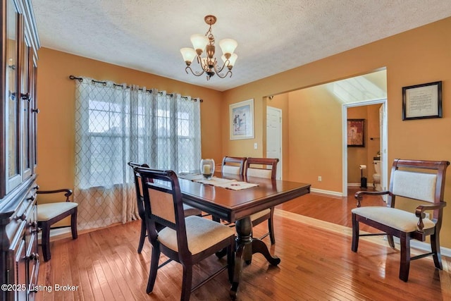 dining space with a textured ceiling, baseboards, light wood finished floors, and a chandelier