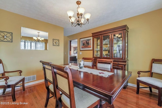 dining area with a textured ceiling, an inviting chandelier, and light wood finished floors