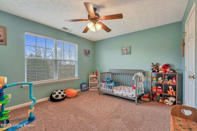 bedroom with visible vents, baseboards, a nursery area, a textured ceiling, and carpet flooring