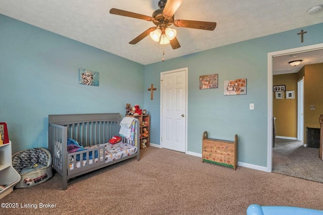 bedroom featuring carpet flooring, a textured ceiling, a crib, and baseboards