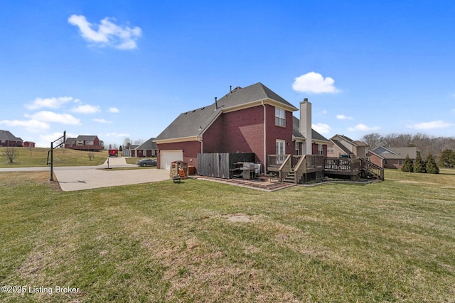 back of property with driveway, a wooden deck, a yard, a chimney, and brick siding