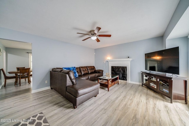 living room featuring a ceiling fan, light wood-style flooring, baseboards, and a tiled fireplace