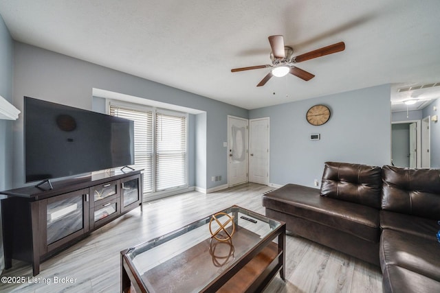 living room featuring ceiling fan, visible vents, baseboards, light wood-style floors, and attic access