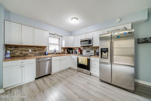 kitchen featuring stainless steel appliances, decorative backsplash, white cabinetry, a sink, and light wood-type flooring