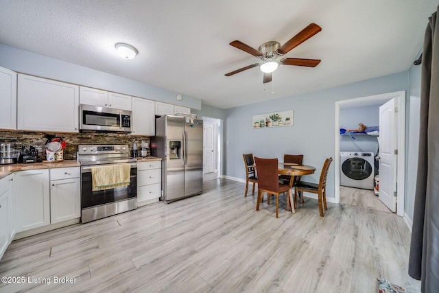 kitchen with light wood finished floors, tasteful backsplash, appliances with stainless steel finishes, white cabinetry, and washer / dryer