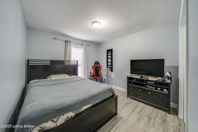 bedroom with light wood-style floors, a textured ceiling, and baseboards