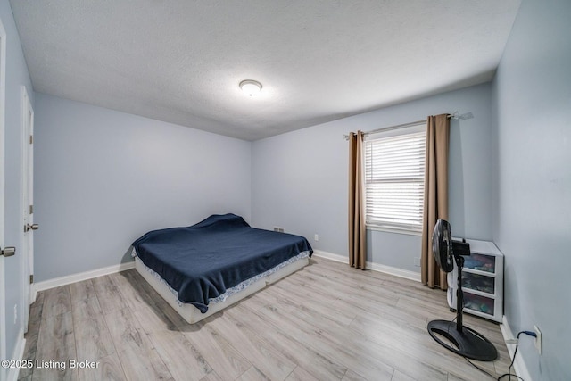 bedroom featuring a textured ceiling, light wood-type flooring, and baseboards