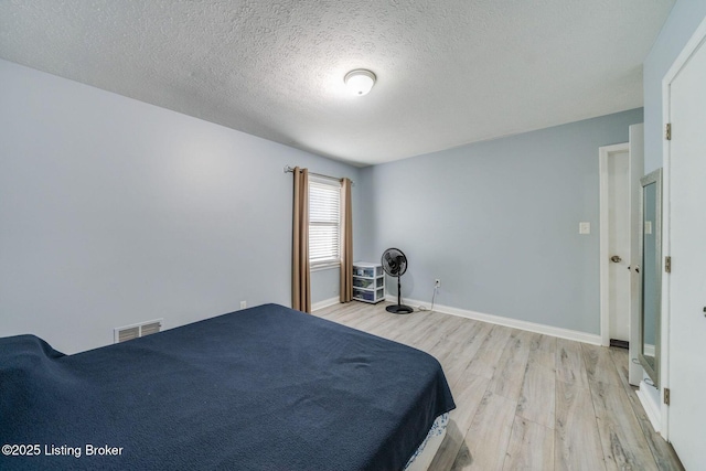 bedroom featuring baseboards, a textured ceiling, visible vents, and light wood-style floors