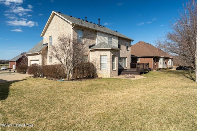 rear view of property with a deck, an attached garage, brick siding, a yard, and roof with shingles