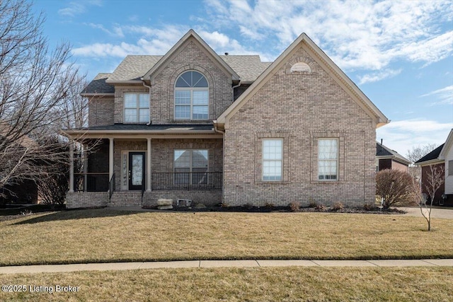 traditional-style home featuring a shingled roof, a porch, a front lawn, and brick siding