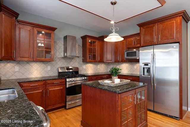 kitchen featuring pendant lighting, decorative backsplash, appliances with stainless steel finishes, light wood-style floors, and wall chimney exhaust hood