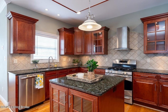 kitchen featuring a sink, appliances with stainless steel finishes, wall chimney exhaust hood, light wood finished floors, and decorative light fixtures