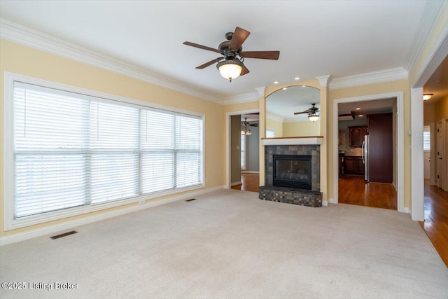 unfurnished living room with a ceiling fan, visible vents, carpet, a glass covered fireplace, and crown molding