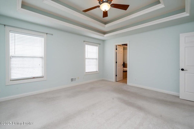 carpeted spare room with ceiling fan, visible vents, baseboards, a raised ceiling, and crown molding