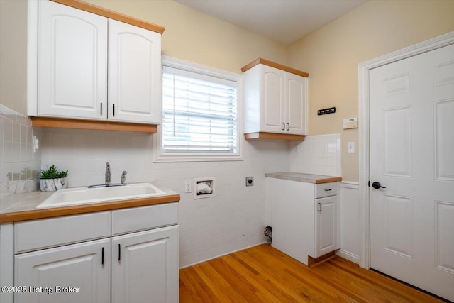 clothes washing area with hookup for an electric dryer, washer hookup, a sink, light wood-style floors, and cabinet space