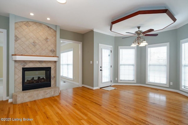 unfurnished living room featuring baseboards, ceiling fan, ornamental molding, wood finished floors, and a fireplace