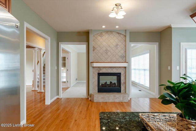 unfurnished living room featuring light wood-style flooring, a fireplace, baseboards, ornamental molding, and stairway