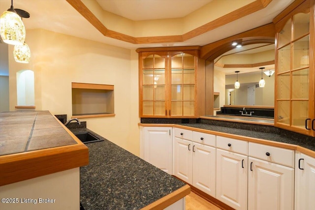 kitchen featuring arched walkways, a sink, glass insert cabinets, and white cabinets