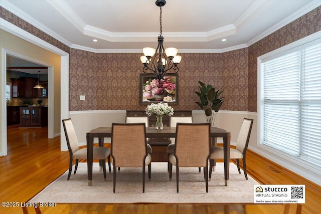 dining space with wallpapered walls, wainscoting, wood finished floors, a tray ceiling, and a notable chandelier