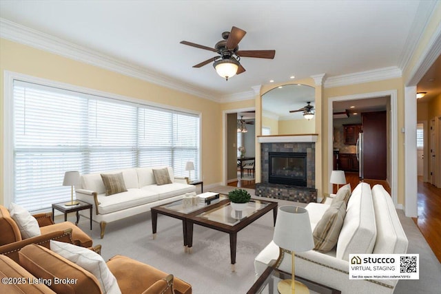 living room featuring ornamental molding, a glass covered fireplace, baseboards, and a ceiling fan