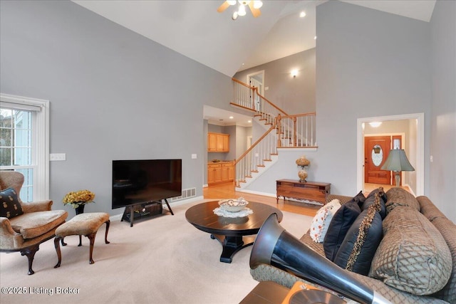 living area with high vaulted ceiling, light colored carpet, visible vents, baseboards, and stairway