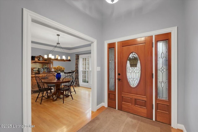 entrance foyer with ornamental molding, a notable chandelier, light wood-style flooring, and baseboards