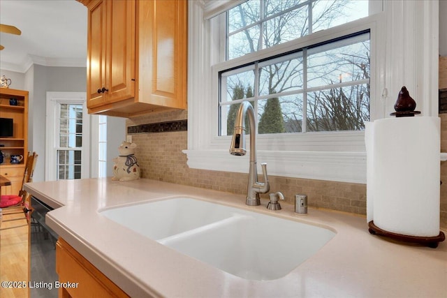 kitchen featuring dishwashing machine, a sink, light countertops, backsplash, and crown molding