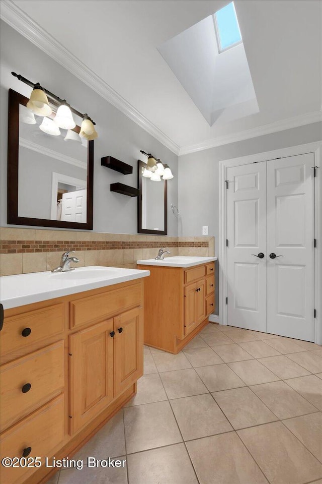 bathroom featuring a skylight, two vanities, ornamental molding, a sink, and tile patterned flooring