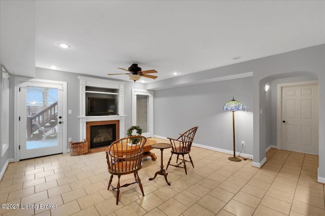 dining room featuring light tile patterned floors, baseboards, arched walkways, a tile fireplace, and recessed lighting