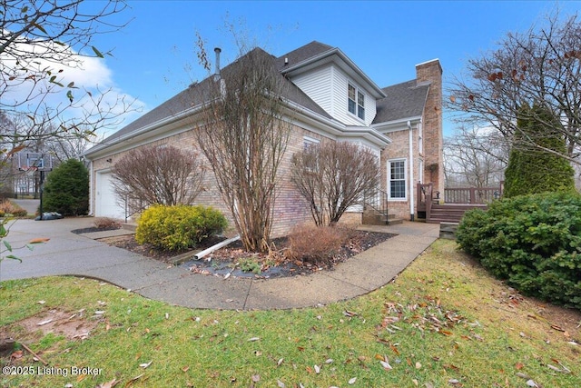 view of side of property with driveway, brick siding, a chimney, and an attached garage