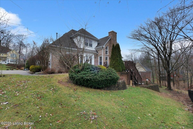 view of side of property featuring stairs, a yard, brick siding, and a chimney