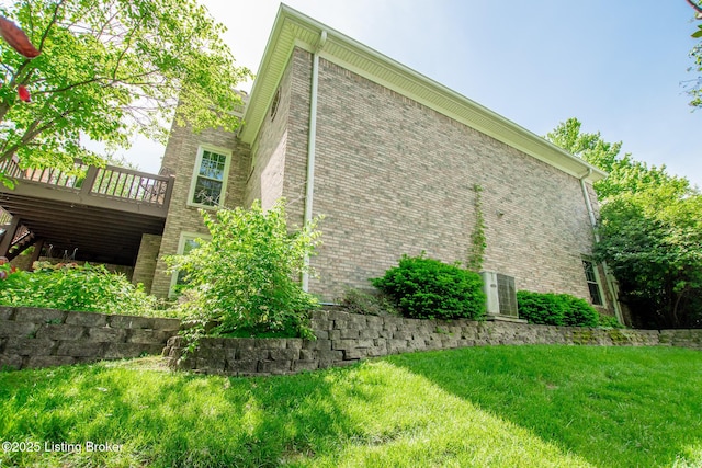 view of side of home with brick siding, a yard, and a deck