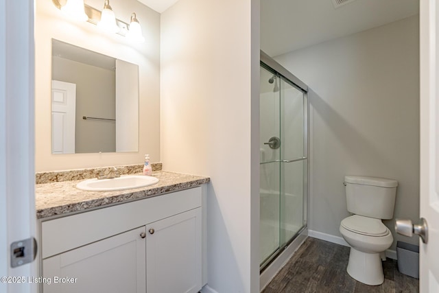 bathroom featuring toilet, wood finished floors, vanity, baseboards, and a stall shower