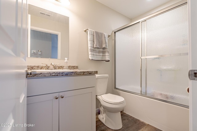 bathroom featuring visible vents, toilet, shower / bath combination with glass door, wood finished floors, and vanity