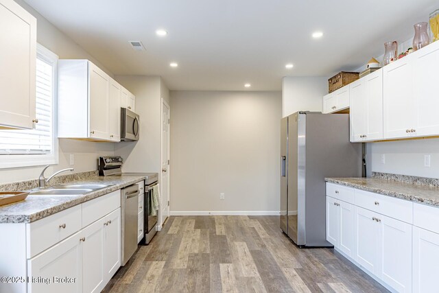 kitchen with light wood finished floors, white cabinets, appliances with stainless steel finishes, a sink, and recessed lighting