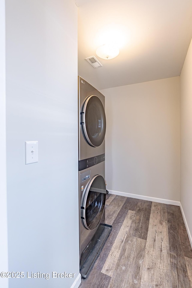 laundry area featuring laundry area, baseboards, visible vents, stacked washer / drying machine, and wood finished floors