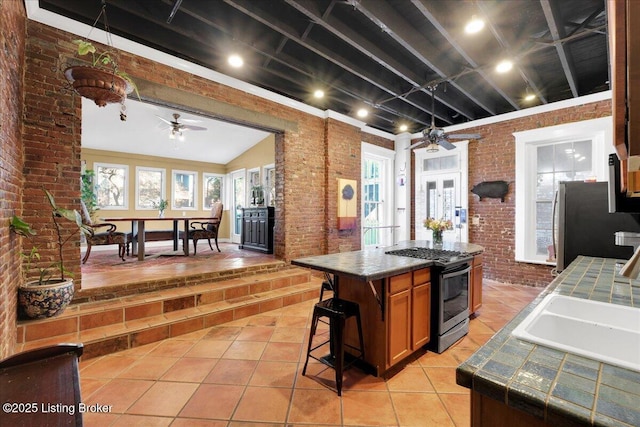 kitchen featuring stainless steel appliances, brick wall, a sink, a ceiling fan, and tile counters