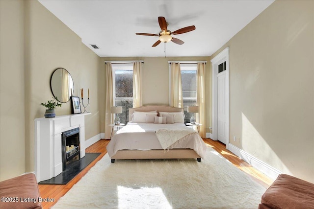 bedroom featuring a fireplace, visible vents, light wood-style flooring, ceiling fan, and baseboards