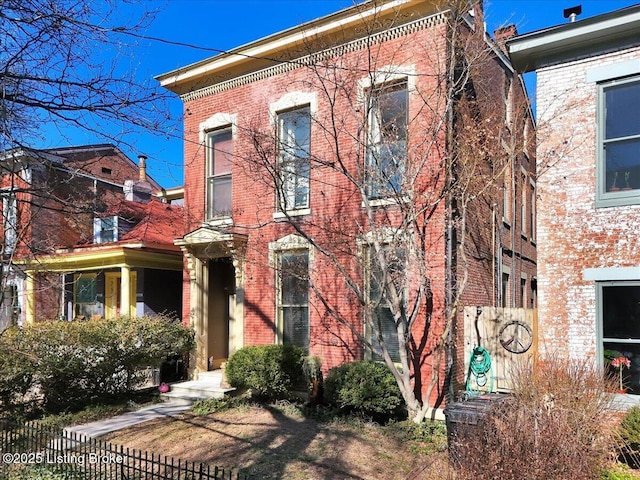 italianate-style house featuring brick siding and fence