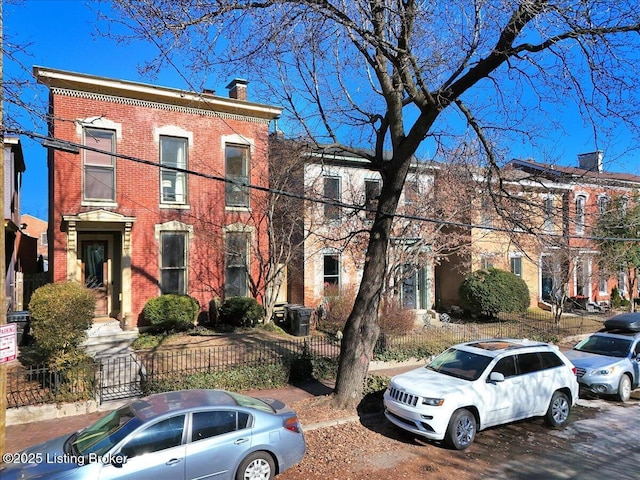 view of front of property with brick siding, a fenced front yard, and a chimney