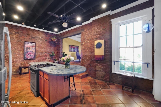 kitchen with ceiling fan, brick wall, a kitchen island, a kitchen breakfast bar, and range with gas cooktop