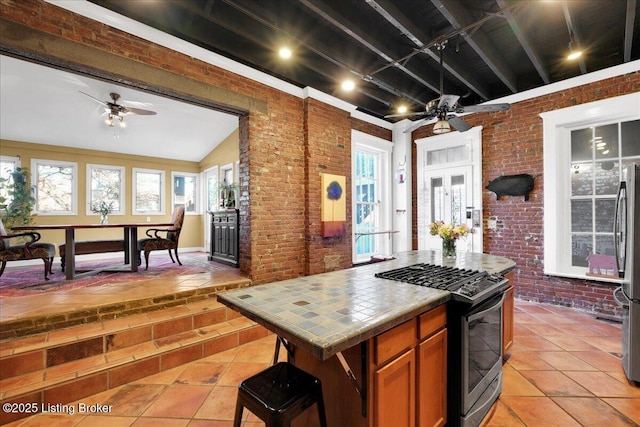 kitchen with tile counters, freestanding refrigerator, ceiling fan, brick wall, and gas range