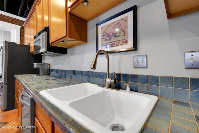 kitchen with tile countertops, brown cabinets, stainless steel appliances, a sink, and light tile patterned flooring