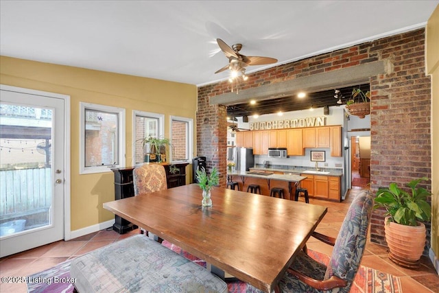 dining area with brick wall, baseboards, ceiling fan, and light tile patterned flooring