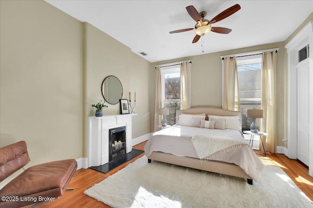 bedroom featuring visible vents, a fireplace with raised hearth, baseboards, and wood finished floors