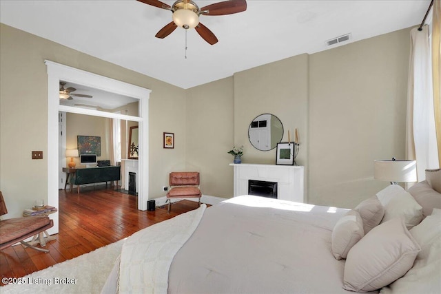 bedroom with hardwood / wood-style flooring, a fireplace, visible vents, baseboards, and a ceiling fan