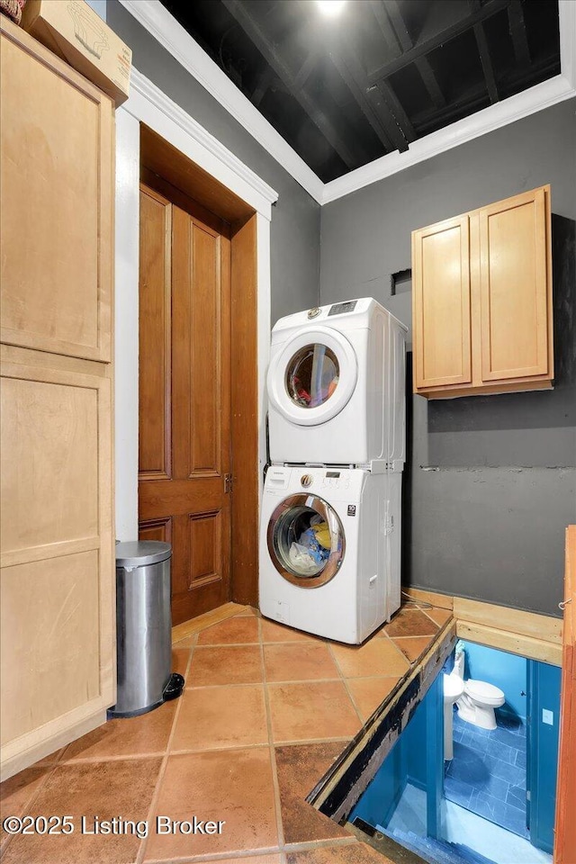 washroom featuring stacked washing maching and dryer, cabinet space, and light tile patterned flooring